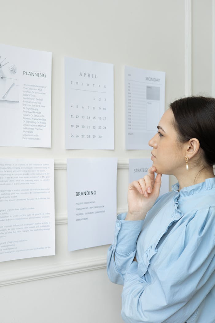 Businesswoman strategizing branding and planning at office wall with papers and calendar.